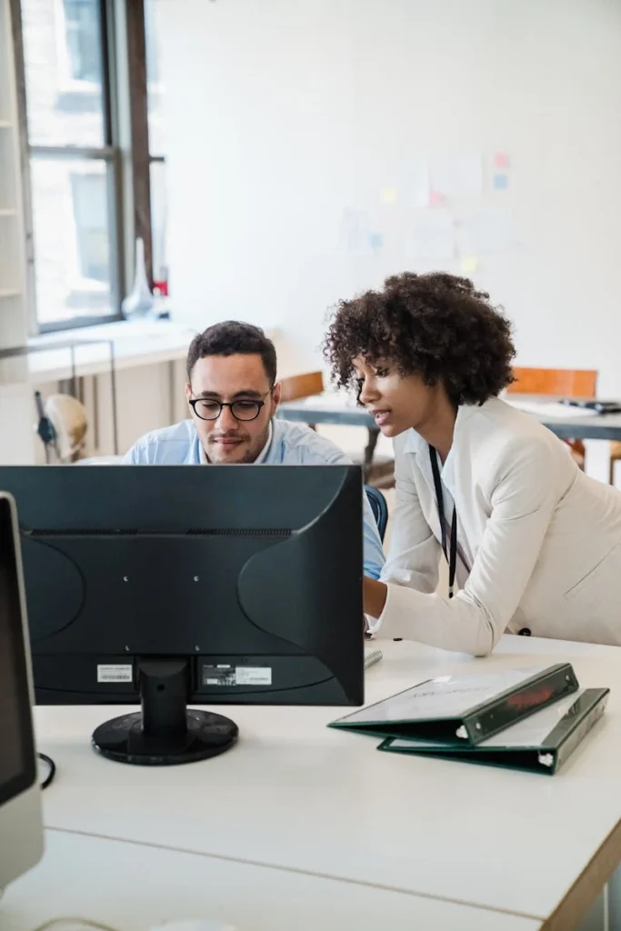 Two professionals collaborate on a computer project in a bright, modern office environment.