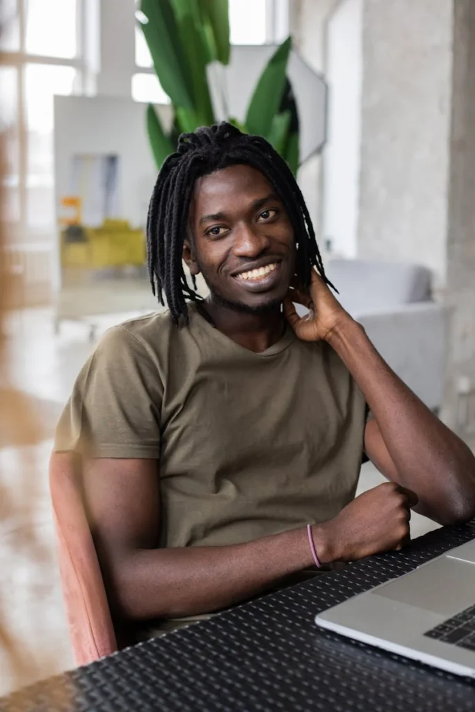 A cheerful African American man working on a laptop in a trendy, well-lit office space.