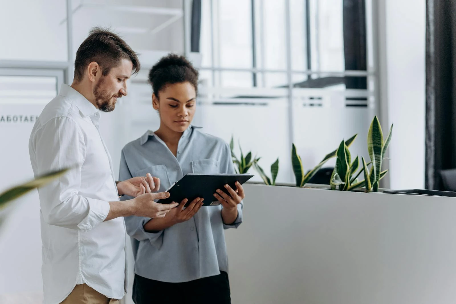 Two coworkers discussing work using a tablet in a modern office setting.