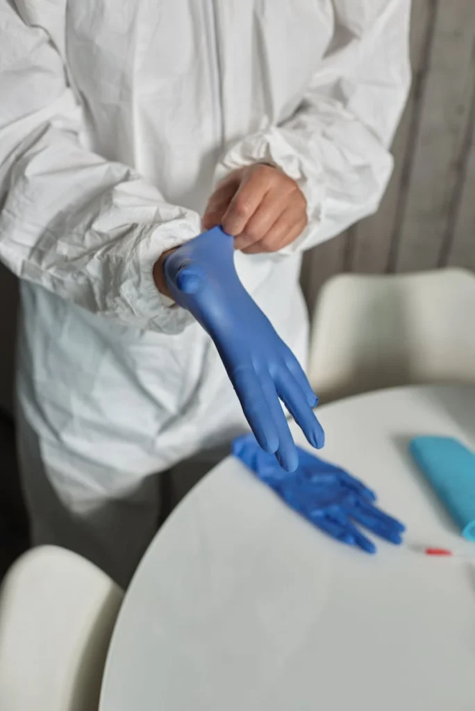Close-up of person in protective suit putting on blue gloves for safety.