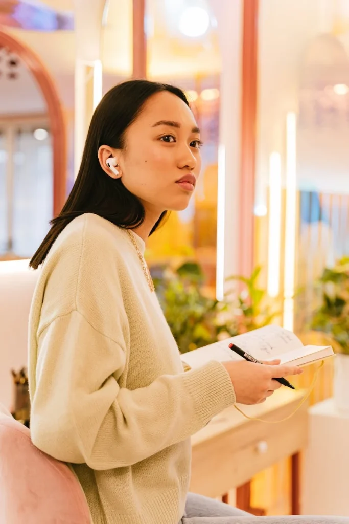 A focused young woman taking notes indoors using a notebook and pen.
