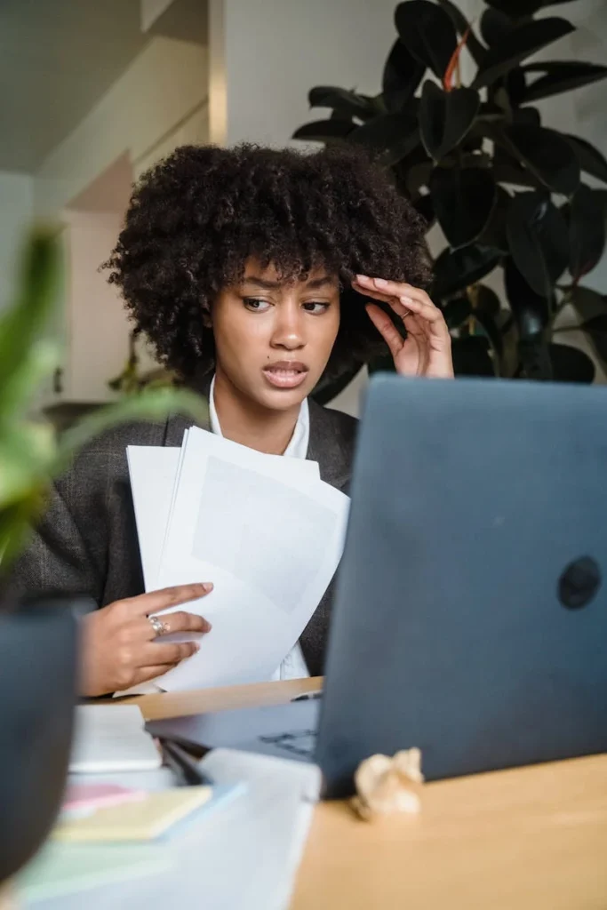 Focused woman feeling stressed while working with laptop and documents at her desk.