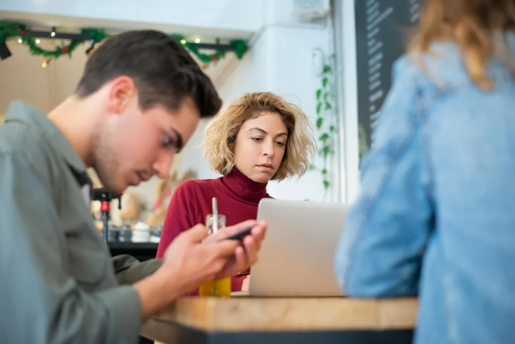 Young professionals collaborating at a cafe, working on laptops and discussing ideas.