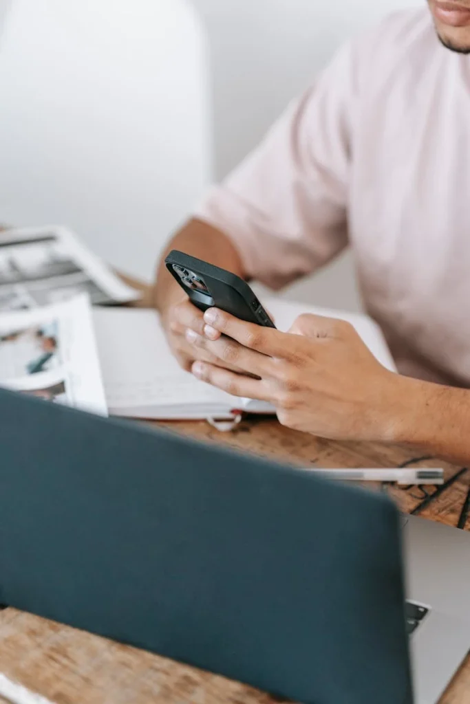 Man multitasking with a smartphone and laptop in a contemporary office setting.