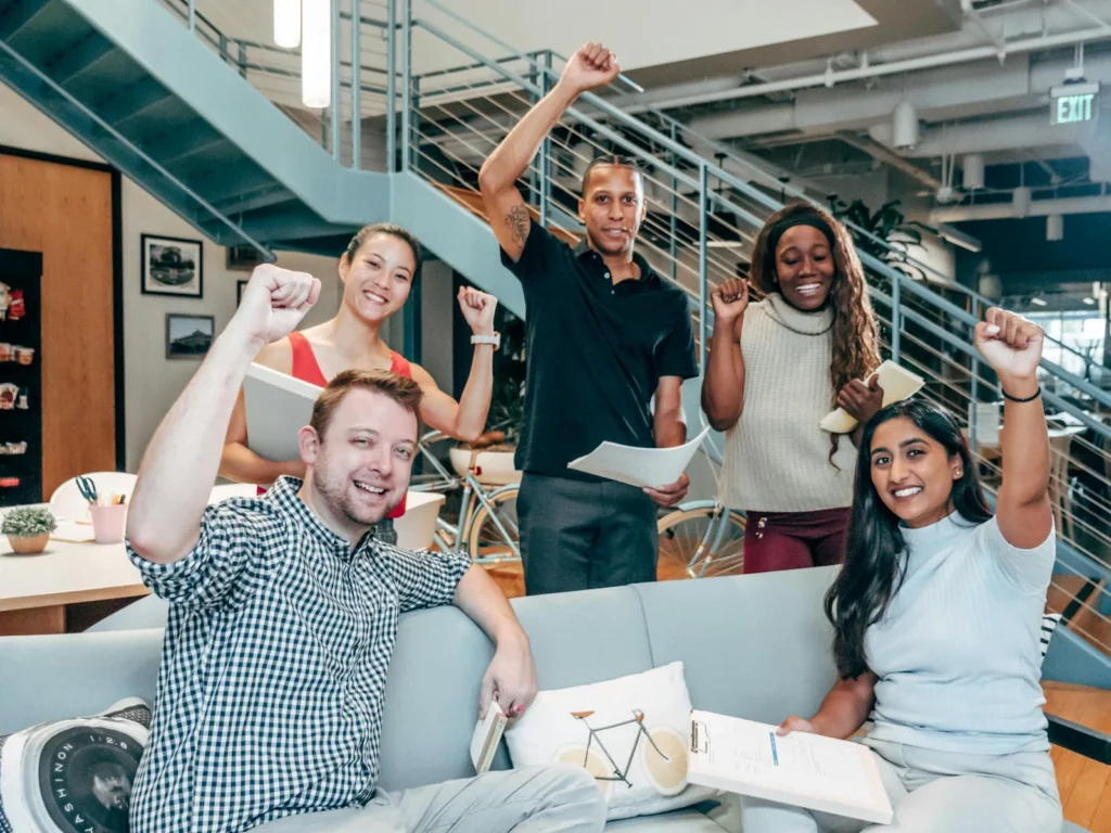 A diverse group of coworkers celebrating success in a modern office setting, showcasing teamwork and collaboration.