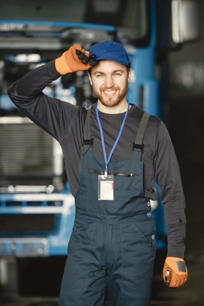 Friendly mechanic in uniform saluting in front of a truck at workplace.