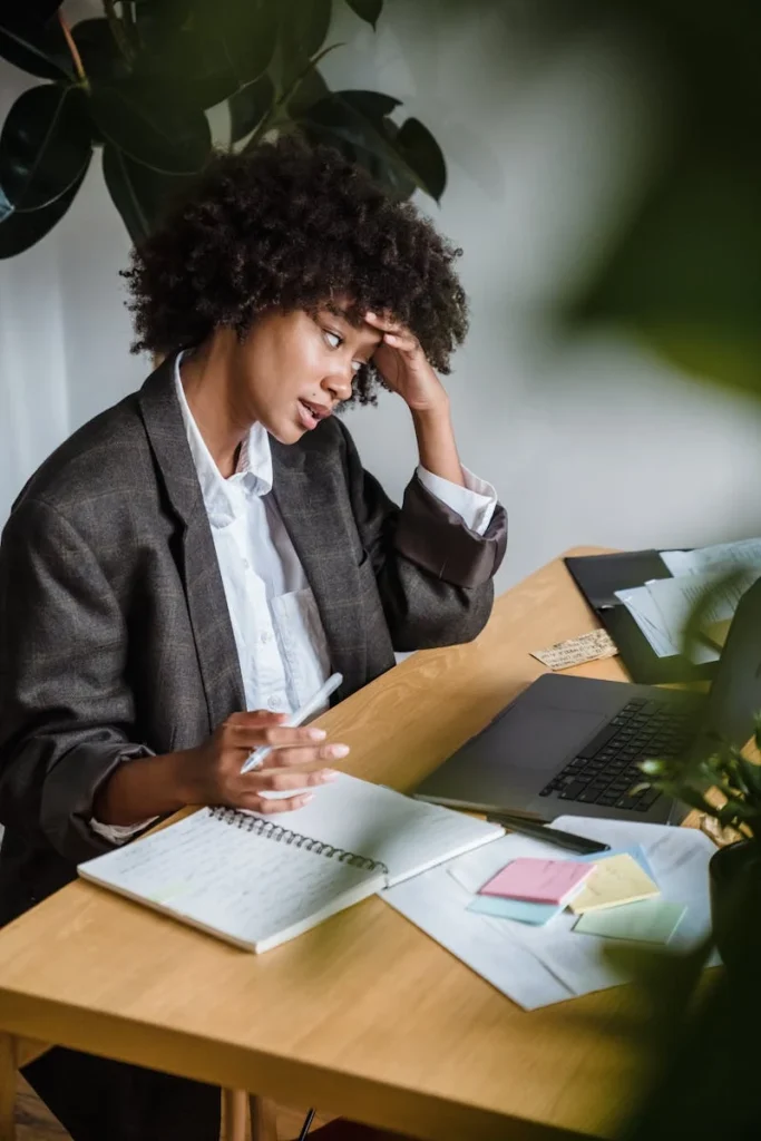 Stressed woman working from home with laptop and notes, focusing on productivity.