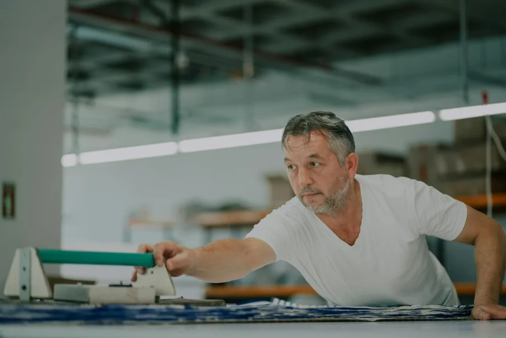 Adult male working with fabric in a textile workshop, showcasing craftsmanship and concentration.