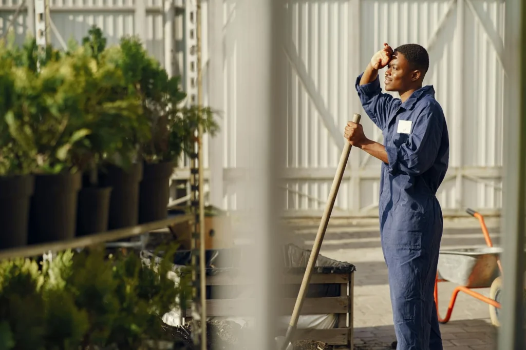 Young gardener working in a greenhouse, surrounded by plants and using a shovel.
