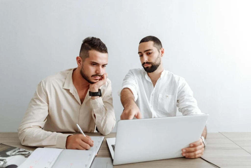 Two businessmen working together on a laptop in an office setting, focusing on a project.