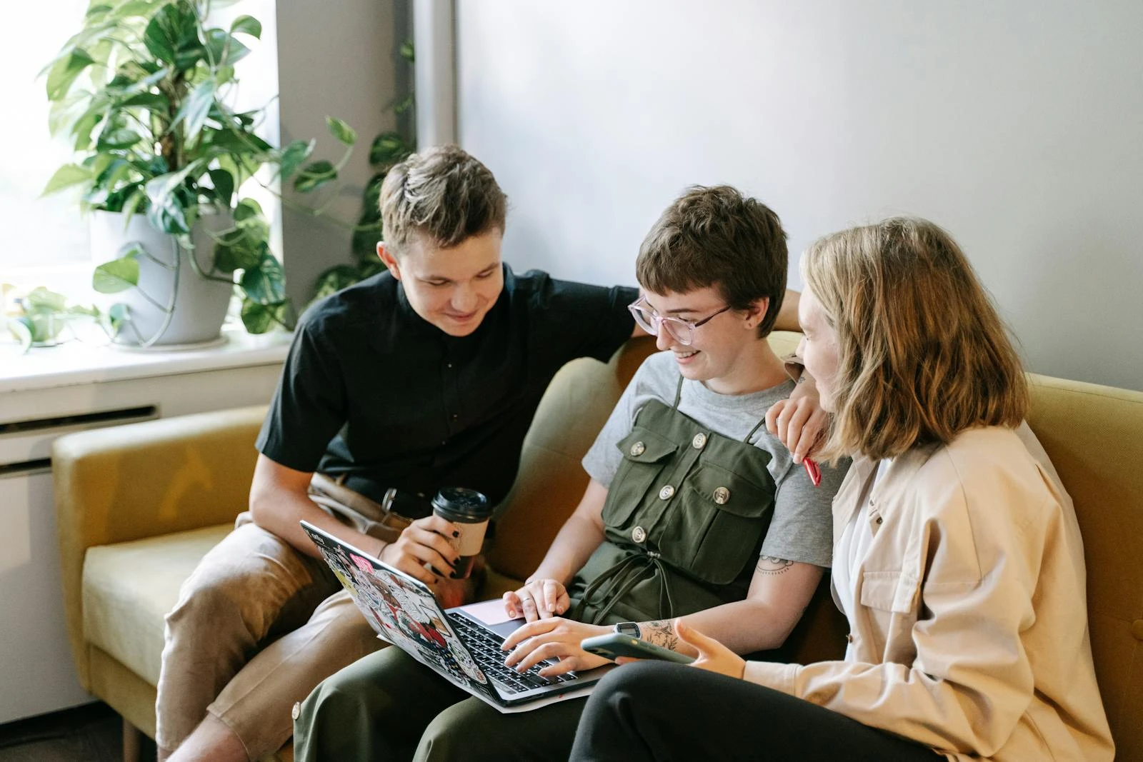 Three young professionals collaborate on a project in a modern indoor workspace, smiling and engaged.