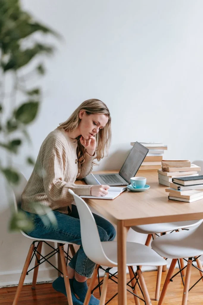 Woman focused on work at home office desk with laptop and books.