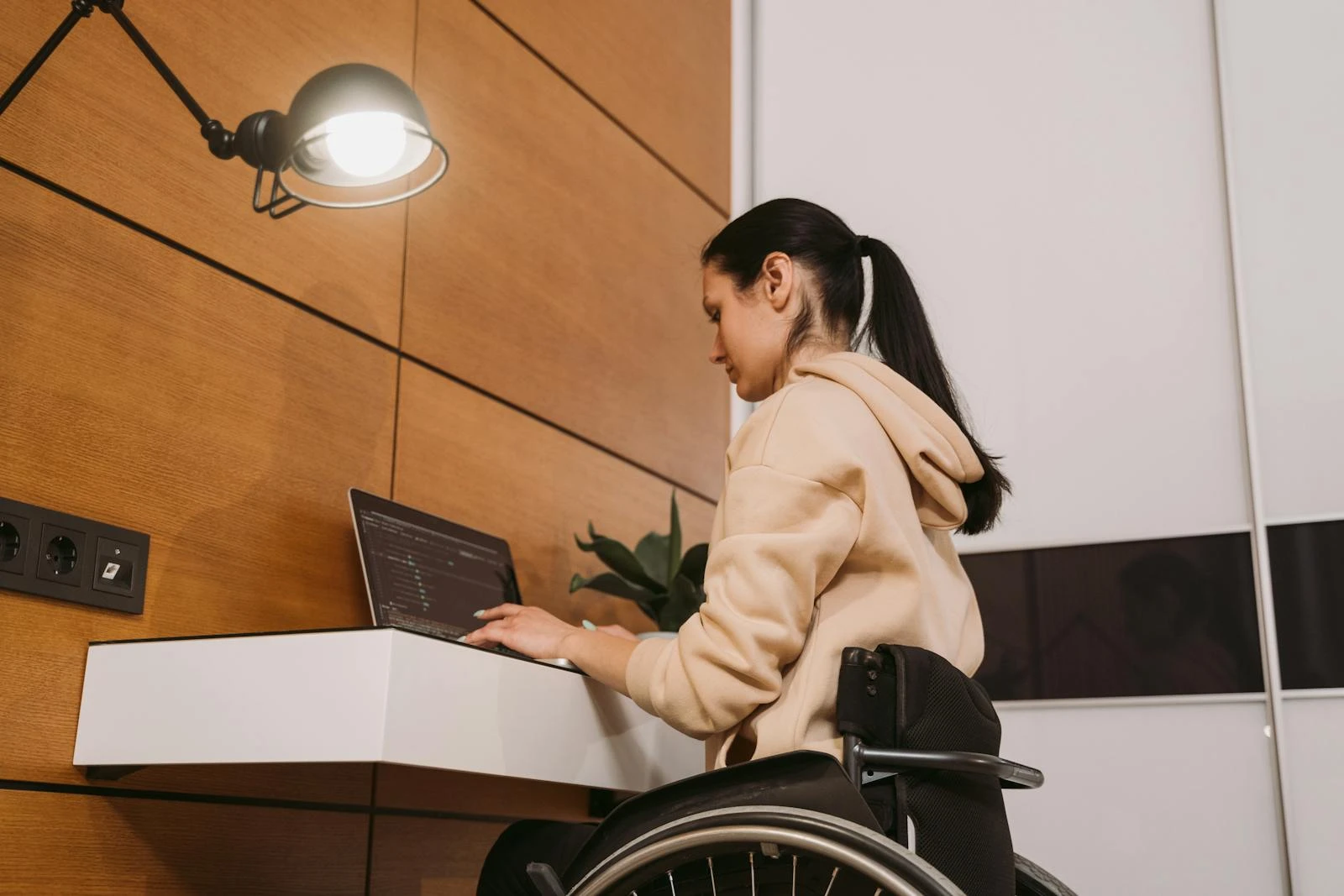 A woman in a wheelchair working on a laptop in a modern interior setting.