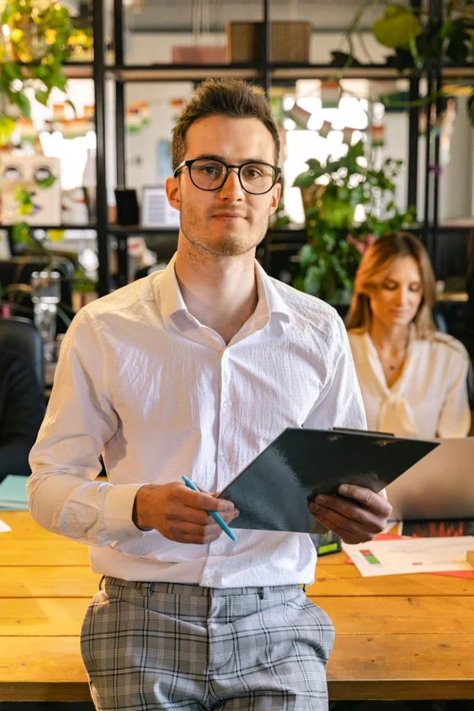 A young professional man in a stylish office holding a clipboard and pen.