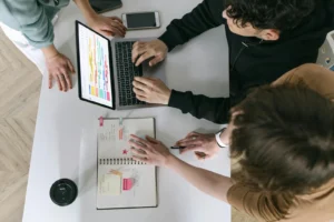 A high-angle view of a team collaborating over a laptop and notebook in a modern office.
