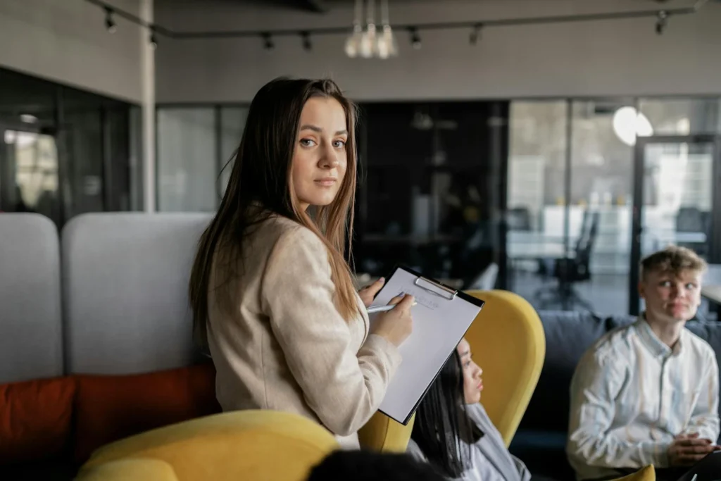 Confident young adult holding a clipboard in a modern office environment.