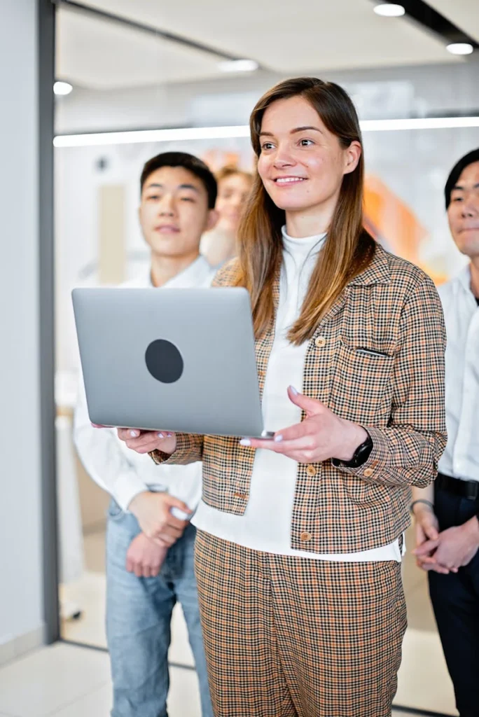 Group of young adults working together in an office setting, focused on a laptop.
