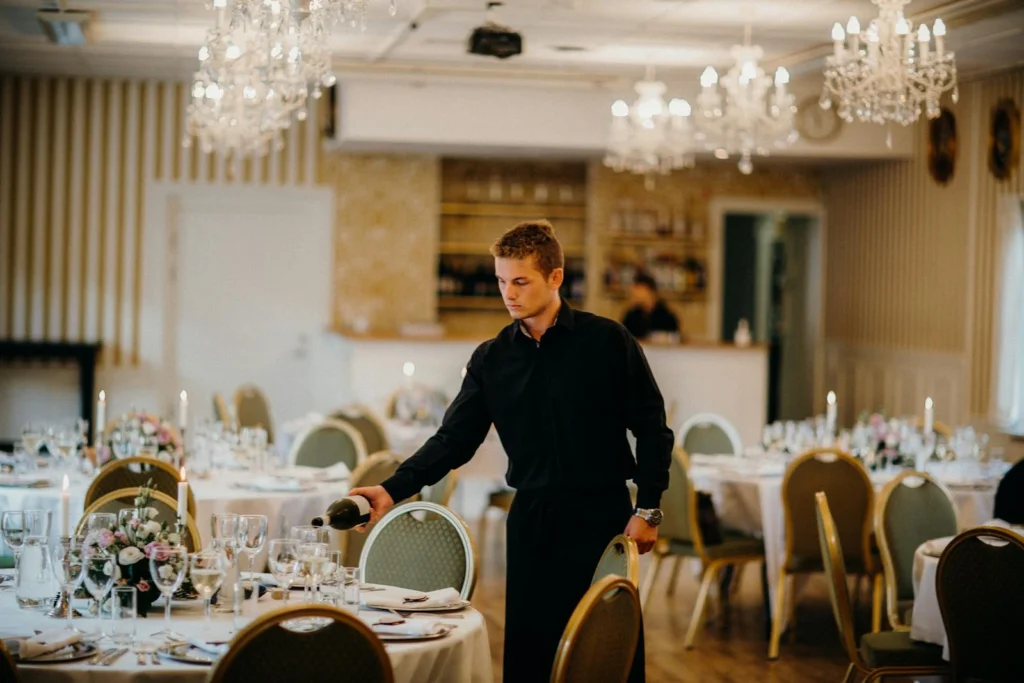 A waiter pours wine in a beautifully set dining room, creating an elegant atmosphere.