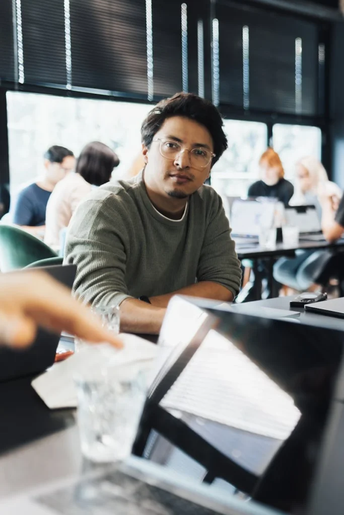 A man focused on work in a modern coworking space with colleagues in the background.