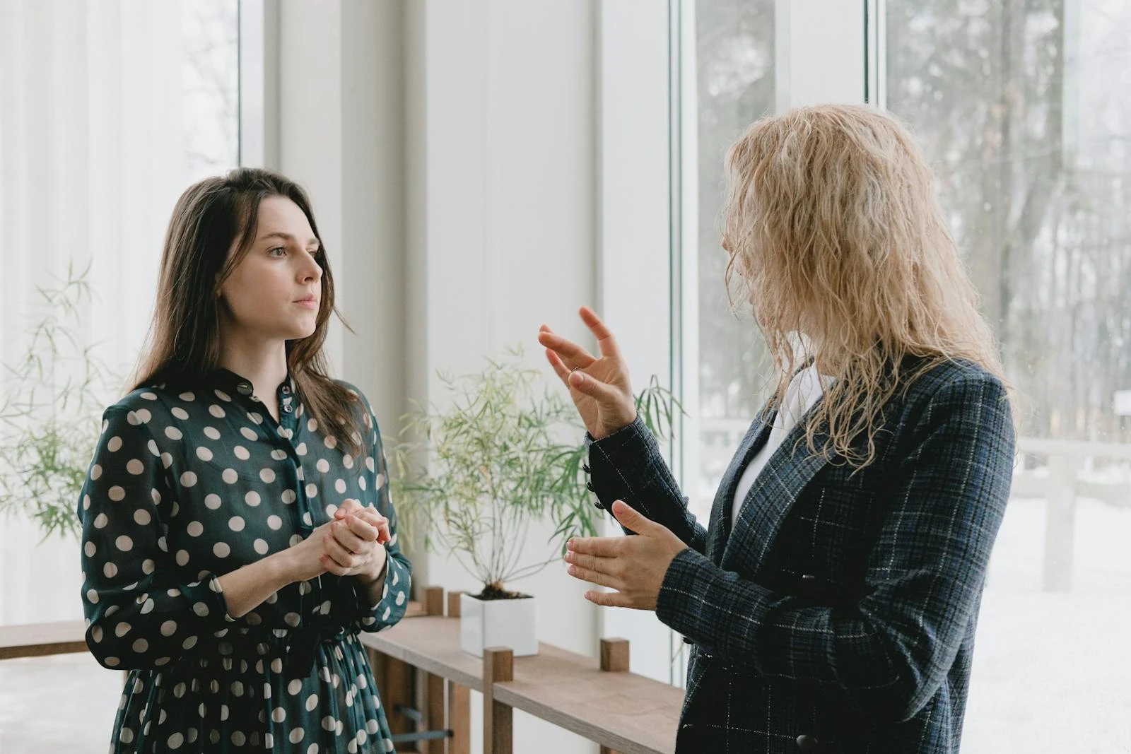 Two women engaging in a professional indoor conversation by a large window.