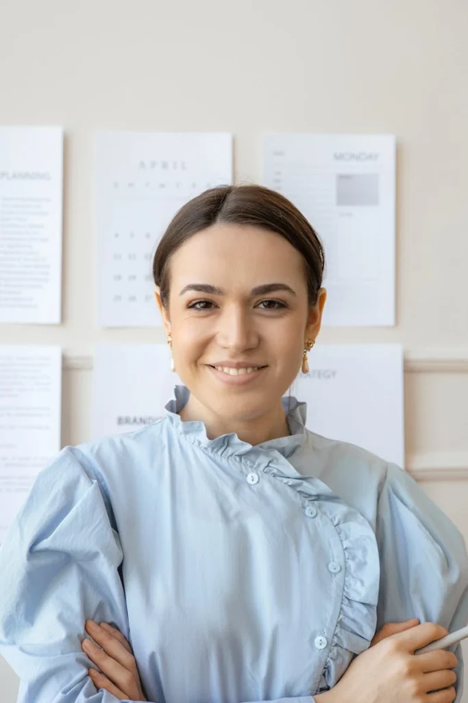 Smiling woman in light blue outfit posing confidently in a modern office setting.